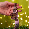 Hand holding a keychain with a bear design against a blurred light background